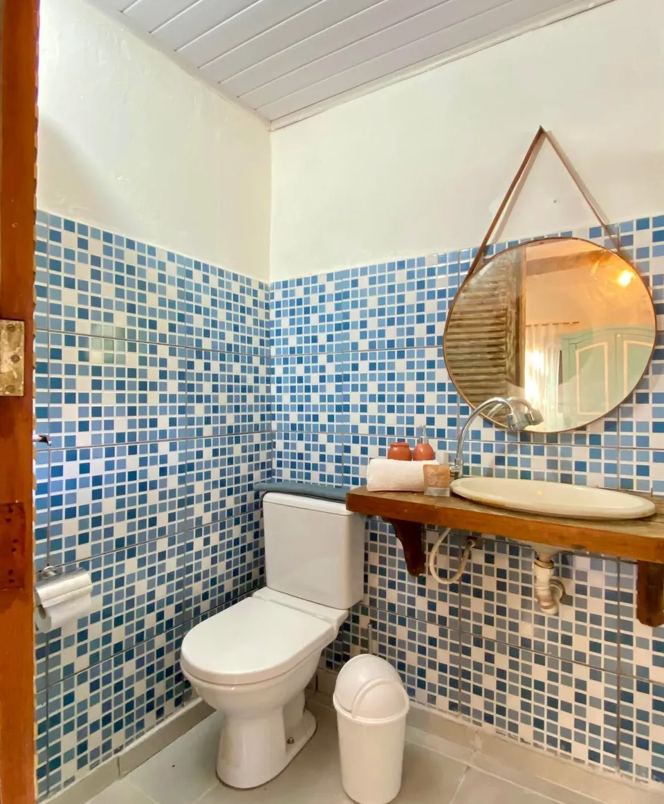 Banheiro da suíte Espada com azulejos azuis e espelho redondo
